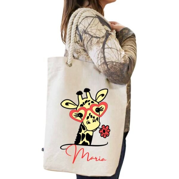 Tote bag blanco de algodón con asa de cuerda blanca y personalizado con la imagen "cuqui" de una jirafa con gafas y una flor de color rojo conjuntamente con el nombre que se quiera personalizar tambien en el mismo color rojo.