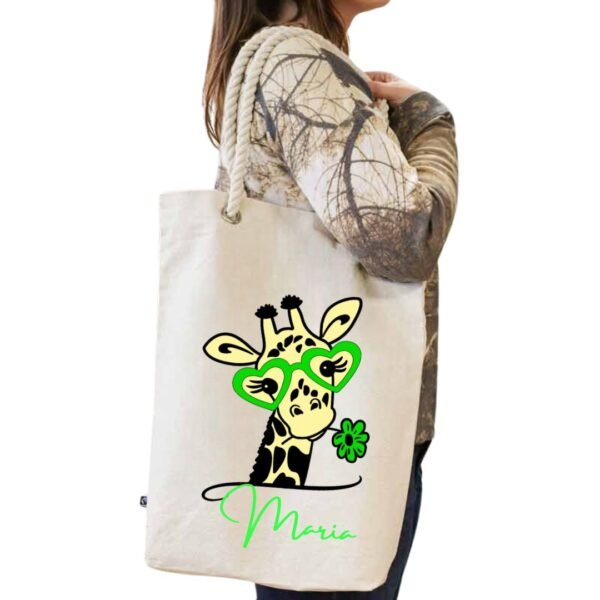 Tote bag blanco de algodón con asa de cuerda blanca y personalizado con la imagen "cuqui" de una jirafa con gafas y una flor de color verde conjuntamente con el nombre que se quiera personalizar tambien en el mismo color verde.