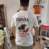 Hombre con camiseta blanca de España Campeones del Mundo 2026, diseño trasero de toro bravo y capote rojo.